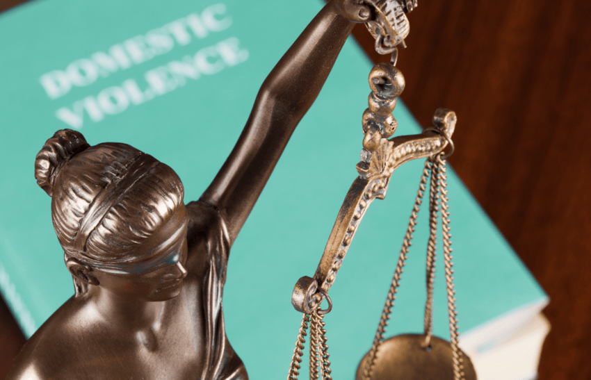 Statue of Lady Justice with scales in front of a book titled Domestic Violence representing legal protection in divorce cases