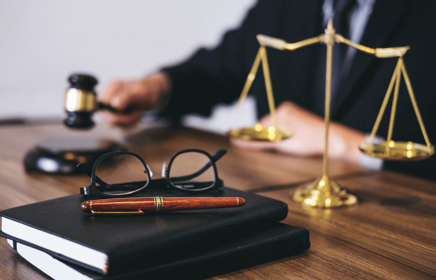 A judge holding a gavel and some law books and a scale present on table.