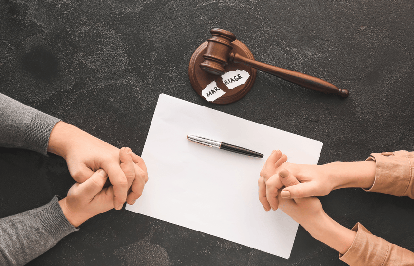 A gavel, paper and pen placed on a table and two individuals' hands.